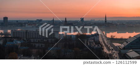 Serene sunrise over Riga, Latvia, featuring St. Peter's Church, Riga Cathedral, Vansu Bridge, and the National Library by the Daugava River. 126112599