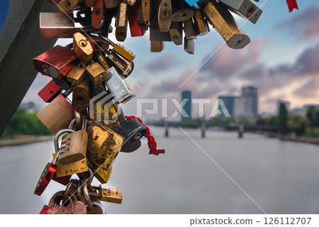 Colorful love locks adorn a metal structure, with the Main River, a bridge, and modern high rise buildings in Frankfurt, Germany, in the background. Colorful love locks adorn a metal structure, with the Main River, a bridge, and modern high rise buildings in Frankfurt, Germany, in the background. 126112707