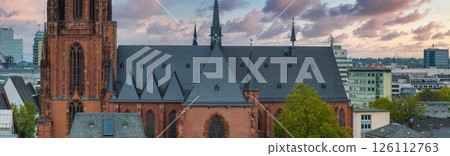 Frankfurt Cathedral's Gothic architecture contrasts with modern buildings under a pink and orange sunset sky, highlighting the city's historic and urban blend. Frankfurt Cathedral's Gothic architecture contrasts with modern buildings under a pink and orange sunset sky, highlighting the city's historic and urban blend. 126112763