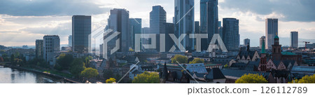 Aerial view of Frankfurt, Germany, featuring the Commerzbank Tower, modern skyscrapers, the Main River, historic buildings, and lush green trees. 126112789