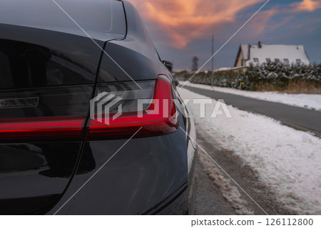 Close up view of the rear left taillight of a black BMW G20 320 parked on a snow lined road, with a house and hedges in a wintry suburban background. Close up view of the rear left taillight of a black BMW G20 320 parked on a snow lined road, with a house and hedges in a wintry suburban background. 126112800