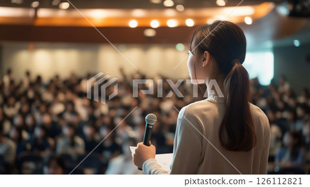 A woman giving a presentation in front of a large audience 126112821