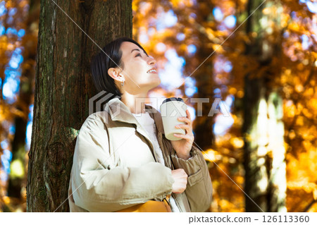 Woman drinking a hot drink while enjoying the autumn leaves Lifestyle image Woman drinking a hot drink while enjoying the autumn leaves Lifestyle image 126113360