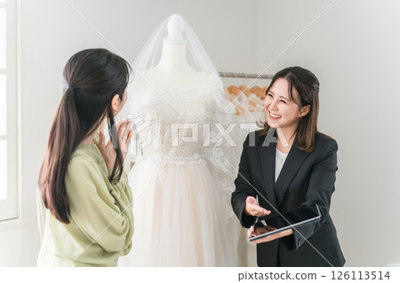 A woman having a meeting with a wedding planner and dress coordinator to choose a dress 126113514