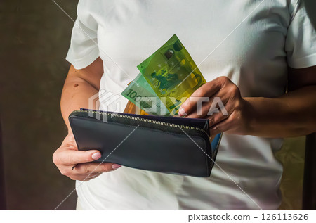 Person is displaying a black wallet with vibrant banknotes in a simple background. High quality photo Person is displaying a black wallet with vibrant banknotes in a simple background. High quality photo 126113626