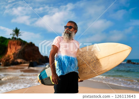 Elderly ethnic man holds surfboard on sunny beach. Senior surfer with beard, sunglasses enjoys ocean waves. Active lifestyle, vibrant summer day, coastline adventure for older generation. Elderly ethnic man holds surfboard on sunny beach. Senior surfer with beard, sunglasses enjoys ocean waves. Active lifestyle, vibrant summer day, coastline adventure for older generation. 126113643