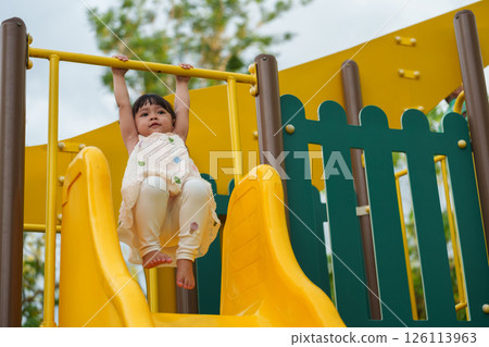 happy toddler girl hanging the yellow bar by her hand at outdoor playground in park happy toddler girl hanging the yellow bar by her hand at outdoor playground in park 126113963
