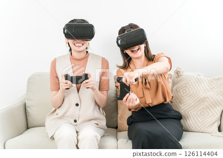 Smiling Asian woman wearing VR goggles and playing games Smiling Asian woman wearing VR goggles and playing games 126114404