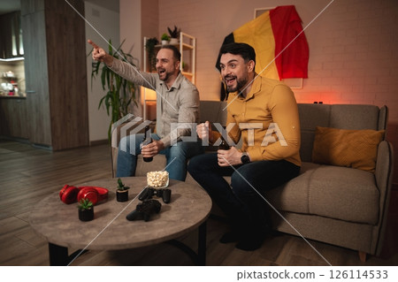 Friends joyfully celebrate a thrilling sports match in a cozy living room while sharing drinks and snacks Friends joyfully celebrate a thrilling sports match in a cozy living room while sharing drinks and snacks 126114533