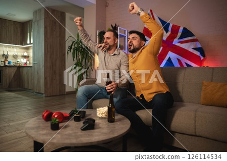 Friends celebrate in cozy living room as they cheer for their favorite team during an exciting sports match on a lively evening Friends celebrate in cozy living room as they cheer for their favorite team during an exciting sports match on a lively evening 126114534