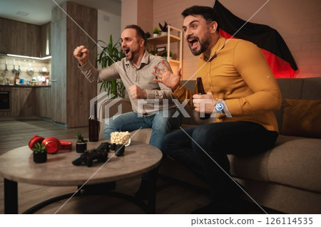 Friends celebrating together while watching a thrilling sports game in their cozy living room during an exciting evening 126114535