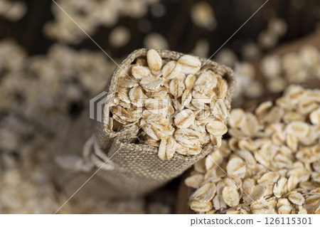 one linen bag with flakes for making porridge, scattered dry cereal flakes from oats, flattened, steamed and dried, closeup one linen bag with flakes for making porridge, scattered dry cereal flakes from oats, flattened, steamed and dried, closeup 126115301