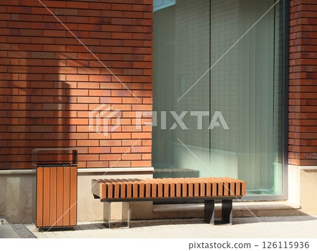 A Modern Urban Bench and a Trash Bin positioned beautifully Against a Brick Wall A Modern Urban Bench and a Trash Bin positioned beautifully Against a Brick Wall 126115936