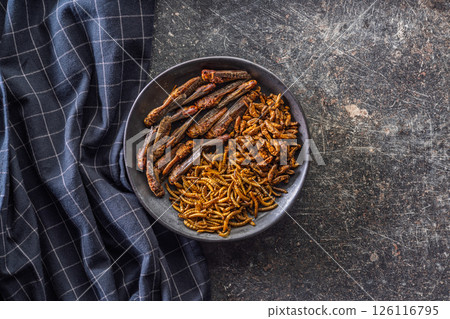 Dried salted insect. Mealworms, grasshoppers and crickets on plate on black table. Top view. Dried salted insect. Mealworms, grasshoppers and crickets on plate on black table. Top view. 126116795