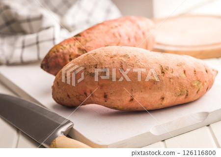 Raw sweet potatoes on cutting board on white table. 126116800