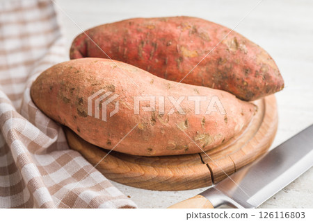 Raw sweet potatoes on cutting board on white table. Raw sweet potatoes on cutting board on white table. 126116803