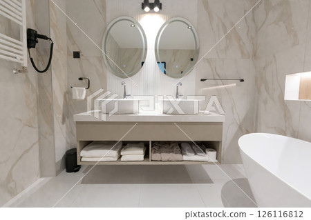 A modern hotel bathroom with double sink, round mirrors and elegant marble interior design 126116812