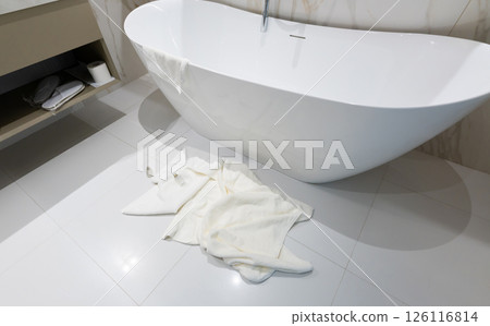 A modern freestanding hotel bathtub with white towels left casually on the floor 126116814