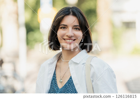 Bright Multiracial Asian Latina Middle Eastern young woman with trendy short hair smiling at the camera in a European street 126116815