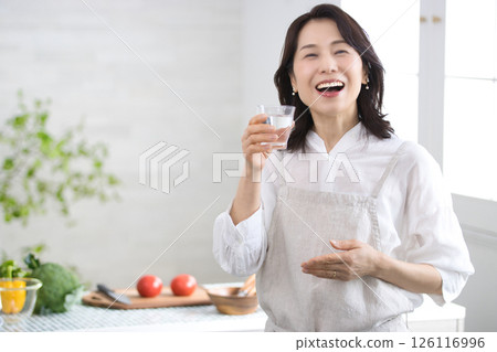 Smiling middle-aged woman drinking water in the kitchen 126116996