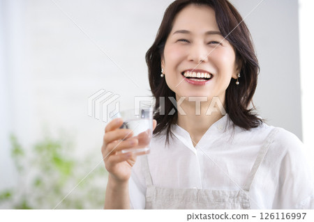 Smiling middle-aged woman drinking water in the kitchen 126116997