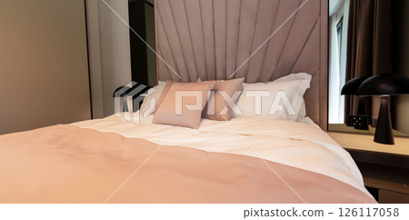 A cozy modern hotel bed with pastel bedding, soft pillows and elegant lighting setup A cozy modern hotel bed with pastel bedding, soft pillows and elegant lighting setup 126117058