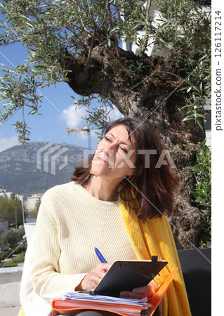 an adult woman on terrace making notes, working with phone an adult woman on terrace making notes, working with phone 126117214