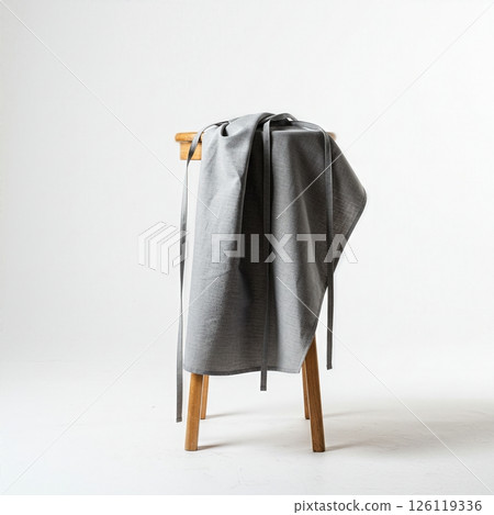 Minimalist Gray Linen Apron Draped Over Wooden Stool in Clean White Studio Setting 126119336