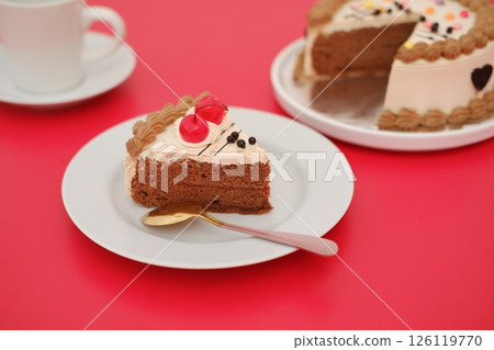 A delicious slice of chocolate cake with cherry topping on a white plate. A delicious slice of chocolate cake with cherry topping on a white plate. 126119770