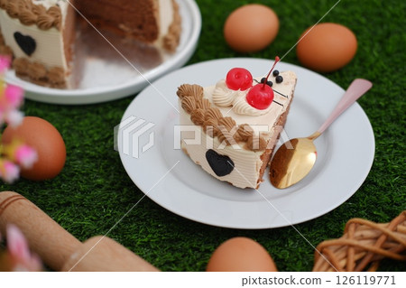 A delicious slice of chocolate cake with cherry topping on a white plate. 126119771