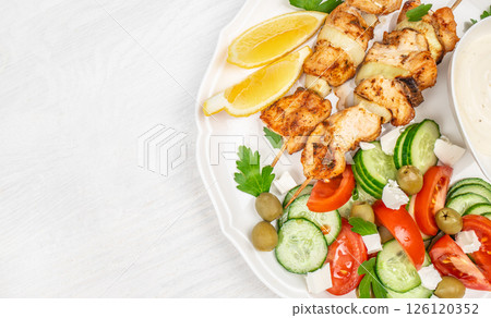 chicken kebab or souvlaki. Mediterranenan healthy lunch greek salad, tzatziki yogurt sauce chicken skewers on white background, top view, copy space 126120352