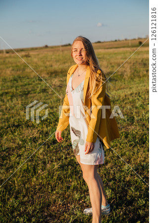 Portrait of a woman in a summer dress on a green field at sunset 126121816