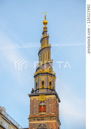 The corkscrew spire of the Church of Our Saviour in Copenhagen rises prominently against a clear blue sky. Its intricate design showcases a blend of architecture and artistry. 126121992
