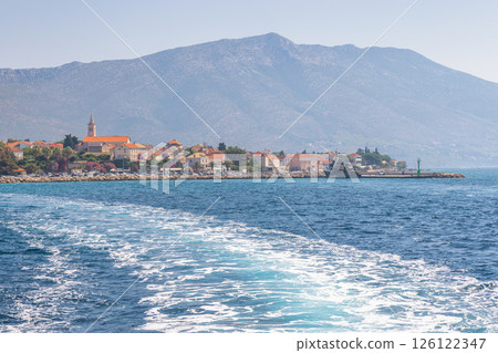 Orebic town at coast of the Peljesac peninsula in Croatia, Europe. Coastal European town with orange rooftops and a backdrop of a mountain viewed from the water. Calm ocean water. 126122347