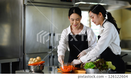 Two female culinary students preparing vegetables during a cooking class in a professional kitchen Two female culinary students preparing vegetables during a cooking class in a professional kitchen 126122604