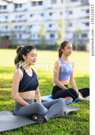 Female friends meditating during a tranquil yoga practice in a sunny park 126122653