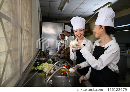 Smiling young chefs learning kitchen hygiene and teamwork in a professional cooking school Smiling young chefs learning kitchen hygiene and teamwork in a professional cooking school 126122679