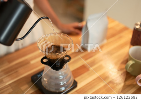 Close up of hand pouring hot water into pour over coffee dripper on a wooden kitchen counter Close up of hand pouring hot water into pour over coffee dripper on a wooden kitchen counter 126122682