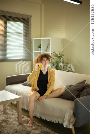 Curly haired woman having conversation on her mobile phone in a living room 126122686