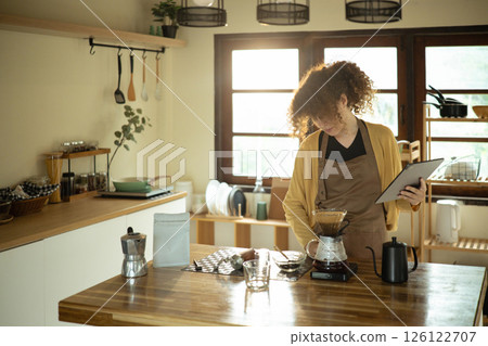 Young woman brewing pour over coffee and using digital tablet in a stylish kitchen 126122707