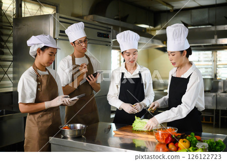 Cooking students attentively watching their teacher demonstrate food preparation techniques Cooking students attentively watching their teacher demonstrate food preparation techniques 126122723