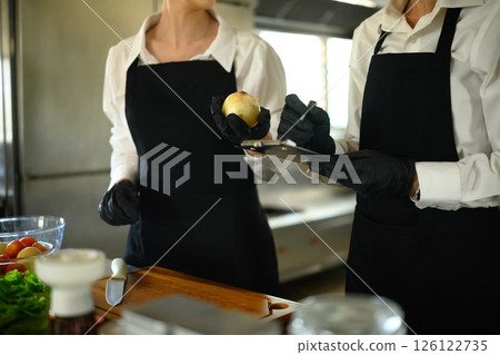 Chefs in training discussing produce quality while documenting kitchen prep procedures 126122735