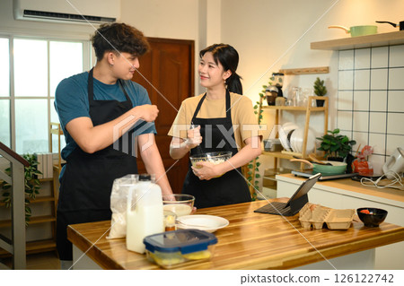 Man and woman wearing aprons mixing ingredients for pancakes in a cozy kitchen 126122742