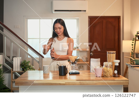 Beautiful woman grinding coffee beans in a kitchen, preparing fresh pour over coffee Beautiful woman grinding coffee beans in a kitchen, preparing fresh pour over coffee 126122747