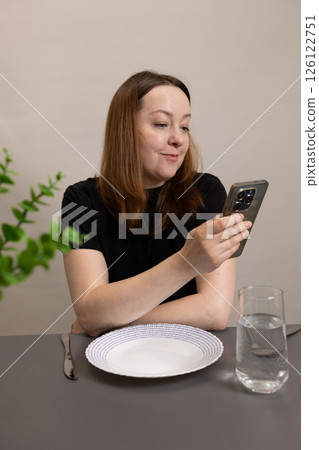 A woman is engaging attentively with her smartphone while sitting at the dining table A woman is engaging attentively with her smartphone while sitting at the dining table 126122751