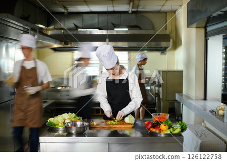 Chef apprentice working on vegetable preparation in a busy kitchen. Chef apprentice working on vegetable preparation in a busy kitchen. 126122758