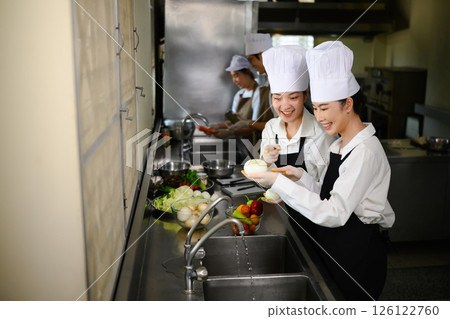 Smiling young chefs learning kitchen hygiene and teamwork in a professional cooking school Smiling young chefs learning kitchen hygiene and teamwork in a professional cooking school 126122760