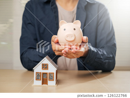 A close-up of hands with a piggy bank and house model, symbolizing saving money, financial planning, and property goals. Highlights mortgage options and homeownership strategies for a secure future. A close-up of hands with a piggy bank and house model, symbolizing saving money, financial planning, and property goals. Highlights mortgage options and homeownership strategies for a secure future. 126122766