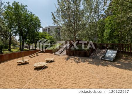 Spacious playground with wooden swings, slides, and shaded natural environment Spacious playground with wooden swings, slides, and shaded natural environment 126122957