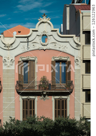 Facade of elegant pink historic building in Barcelona with ornate white decorations and wooden shutters Facade of elegant pink historic building in Barcelona with ornate white decorations and wooden shutters 126122963